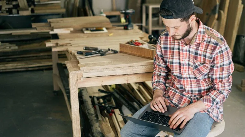 A small-business owner working at a laptop in his woodshop