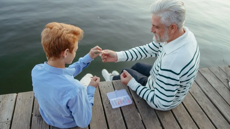 A grandfather and his grandson sitting together on a lake dock